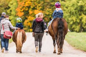 Eltern führen die Pferde der Kinder beim Ausreiten